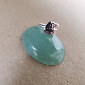 May include: Silver ring with an eagle head design. The ring is displayed on a green stone ring holder.