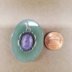 May include: A silver pendant with a purple and white oval gemstone set in a silver bezel. The pendant is about the size of a US penny.