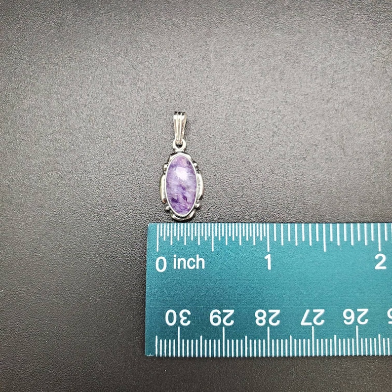 Peut inclure: Un pendentif en argent avec une pierre ovale de couleur violette et blanche. Le pendentif mesure environ 2,5 cm de long et est pr&eacute;sent&eacute; &agrave; c&ocirc;t&eacute; d'une r&egrave;gle.
