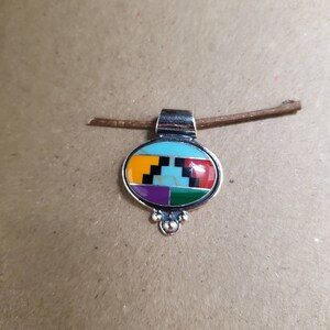 May include: A silver pendant with a colorful geometric design. The pendant is oval shaped and features turquoise, yellow, orange, red, purple, green, and black stones.