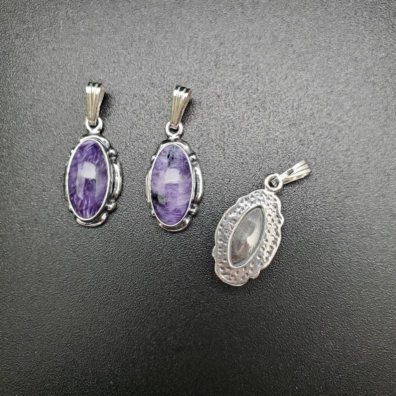 Peut inclure: Trois pendentifs en argent avec des pierres de forme ovale. Deux pendentifs pr&eacute;sentent des pierres violettes et blanches, tandis que le troisi&egrave;me pendentif a une pierre argent&eacute;e.