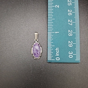 Peut inclure: Un pendentif en argent avec une pierre ovale de couleur violette et blanche. Le pendentif mesure environ 2,5 cm de long.