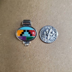 May include: A silver pendant with an oval-shaped turquoise, red, orange, purple, green, and black inlay. The pendant is about the size of a dime.