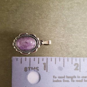 May include: A silver pendant with a purple gemstone set in a silver bezel. The pendant is approximately 1 inch in length.