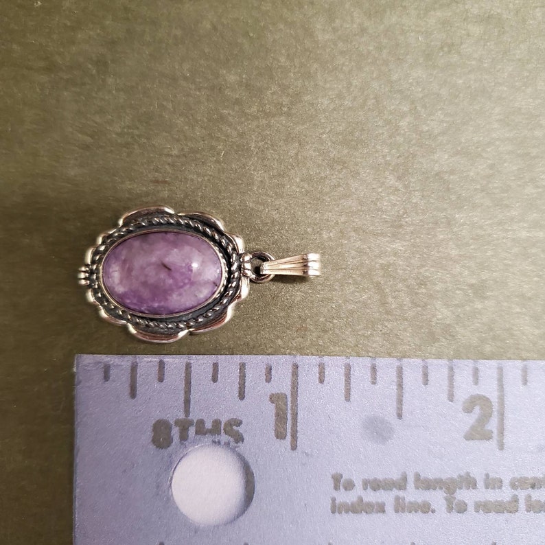 May include: A silver pendant with a purple gemstone set in a silver bezel. The pendant is approximately 1 inch in length.