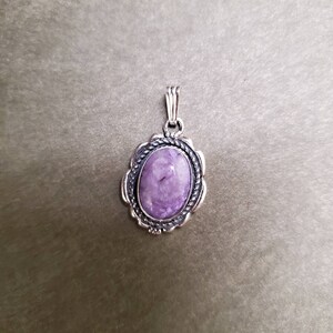 May include: A silver pendant with a purple oval gemstone set in a detailed silver frame.