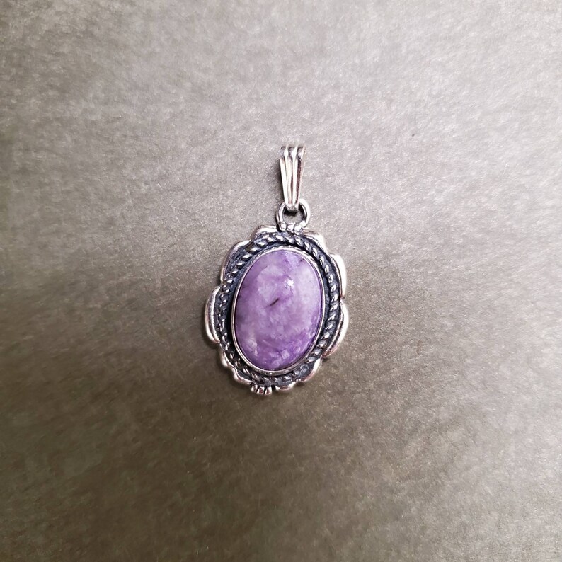 May include: A silver pendant with a purple oval gemstone set in a detailed silver frame.