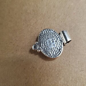 May include: Silver pendant with a textured oval design and a small bead detail. The back of the pendant is stamped with "925" and a star.