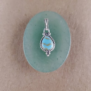 May include: A silver pendant with a light blue and gold teardrop-shaped stone. The pendant is on a green background.