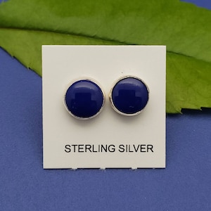 Peut inclure: Deux boucles d'oreilles rondes, bleu cobalt, avec un sertissage en argent sterling. Les boucles d'oreilles sont présentées sur une carte blanche avec l'inscription "STERLING SILVER" en noir.