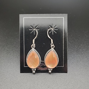 May include: A pair of silver dangle earrings with a pearlescent pink teardrop-shaped stone in each earring.