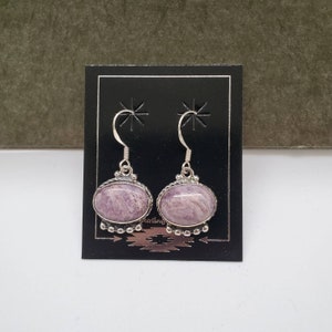 Puede incluir: Un par de pendientes de plata con piedras ovaladas de color morado y blanco. Las piedras tienen un patrón de remolino.