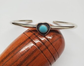 May include: A silver bangle bracelet with a heart-shaped turquoise stone charm.