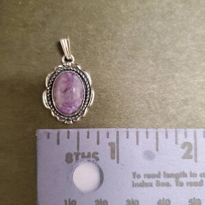 May include: A silver pendant with a purple and white stone set in a silver oval frame. The pendant is about 1 inch in length.
