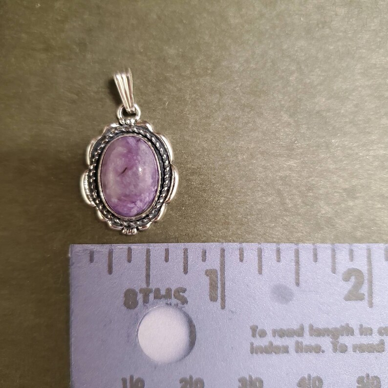 May include: A silver pendant with a purple and white stone set in a silver oval frame. The pendant is about 1 inch in length.