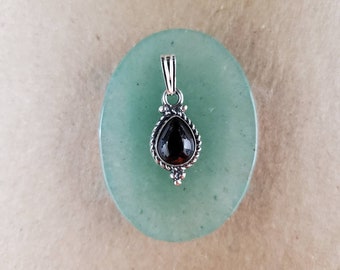 Peut inclure: Un pendentif en argent avec une pierre précieuse noire en forme de larme. Le pendentif est sur un fond vert.
