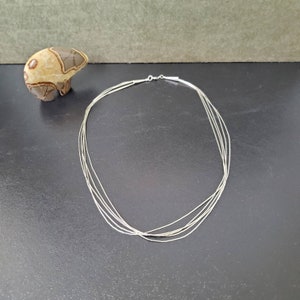 Op de afbeelding: Een zilveren meerrijen ketting met een delicaat kettingontwerp. De ketting is gelaagd met meerdere strengen dunne zilveren ketting, wat een delicate en elegante uitstraling creëert.