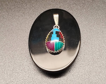 May include: A silver pendant with a teardrop-shaped stone inlaid with colorful stones. The stone is a mix of black, red, green, blue, and turquoise.
