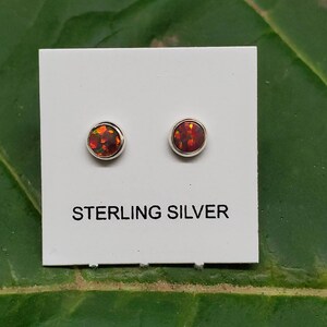 May include: A pair of sterling silver stud earrings with round, red, orange, and yellow opal stones.