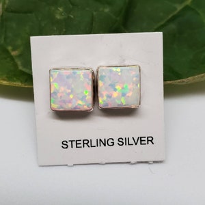 May include: A pair of square-shaped opal earrings set in sterling silver. The opals are iridescent with shades of white, pink, and green.