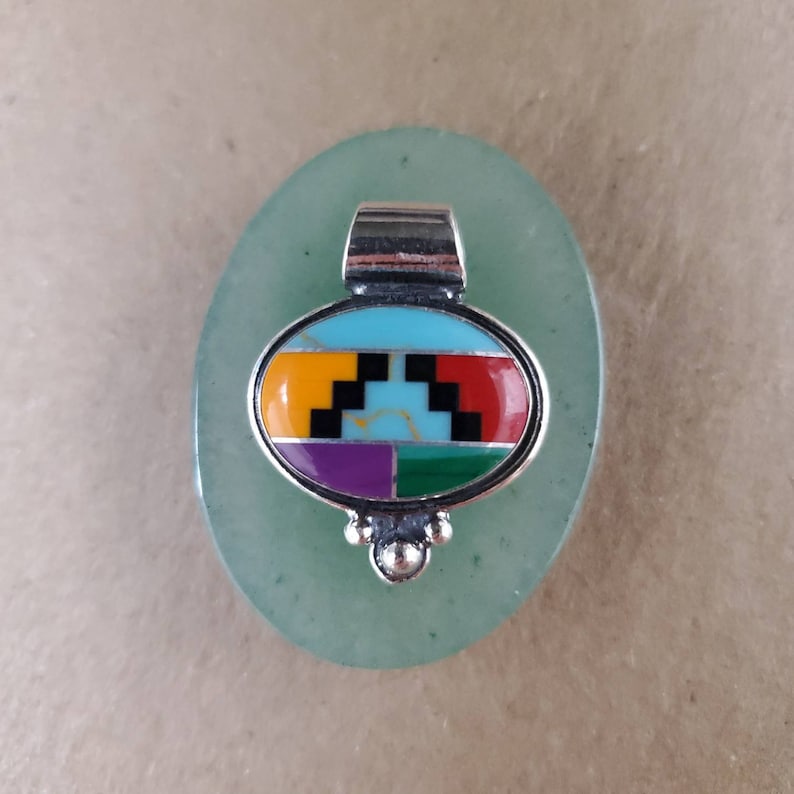 May include: A silver pendant with a turquoise, red, yellow, purple, and green inlay design. The pendant is oval shaped and has a silver bail.