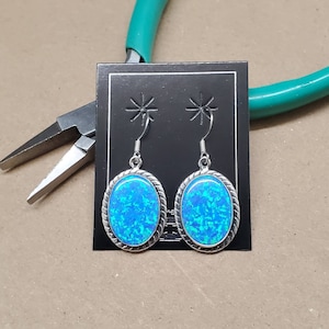 Könnte beinhalten: Ein Paar silberne Ohrringe mit ovalen, blauen Opal-Steinen. Die Ohrringe haben ein seilartiges Design um den Rand des Steins.