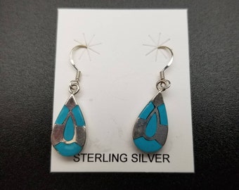 May include: A pair of sterling silver dangle earrings with turquoise inlay. The earrings are teardrop shaped and have a silver hook.
