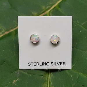 May include: A pair of sterling silver stud earrings with white opal stones. The earrings are displayed on a white card with the text "STERLING SILVER".