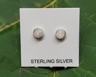 Puede incluir: Un par de pendientes de botón de plata de ley con piedras de ópalo blanco. Los pendientes se muestran en una tarjeta blanca con el texto "STERLING SILVER".