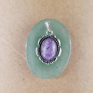 May include: A silver pendant with a purple and white stone set in a decorative silver frame. The pendant is on a green background.