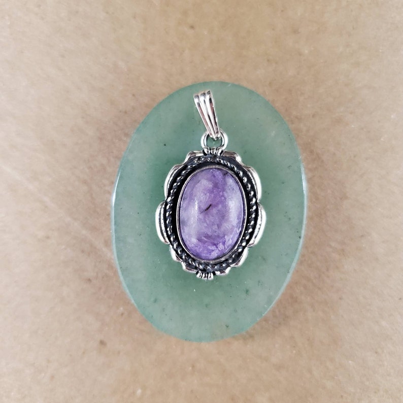 May include: A silver pendant with a purple and white stone set in a decorative silver frame. The pendant is on a green background.