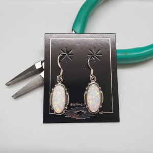 May include: A pair of sterling silver earrings with oval-shaped opal stones. The opals are white with hints of pink and orange.