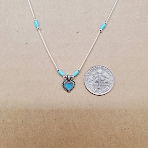 Puede incluir: Un collar de plata con un colgante de corazón turquesa. El collar es del tamaño de una moneda de diez céntimos.
