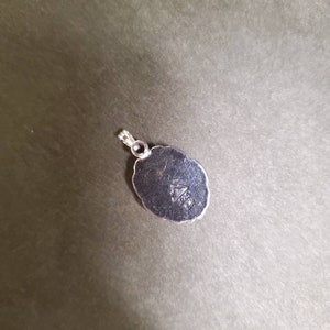 May include: Silver pendant with a detailed oval design. The back of the pendant has a triangle with the inscription "925" inside.