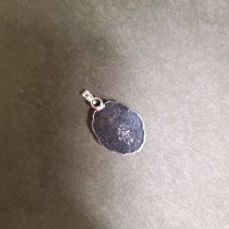 May include: Silver pendant with a detailed oval design. The back of the pendant has a triangle with the inscription "925" inside.