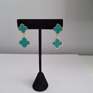 Peut inclure: Une paire de boucles d'oreilles pendantes dorées avec deux breloques en forme de trèfle turquoise sur chaque boucle d'oreille.