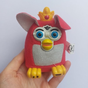 May include: Red plush toy with a yellow crown, blue eyes, and a yellow beak. The toy has a white face and yellow feet. The toy has a McDonald's tag attached to it.