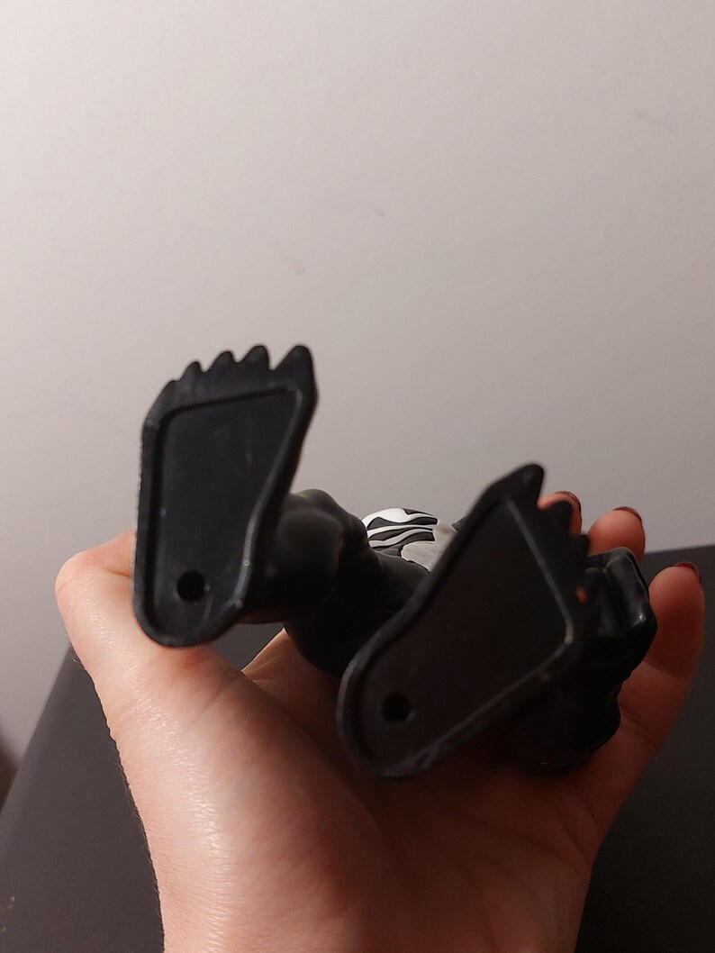 Peut inclure: Une figurine d'action en plastique noir avec un symbole blanc sur la poitrine. La figurine est couch&eacute;e sur le dos, les pieds en l'air.
