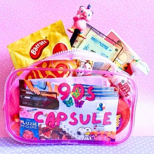 Può includere: Un astuccio rosa trasparente con cerniera pieno di oggetti a tema anni '90. L'astuccio contiene caramelle, una penna con una statuina a forma di maiale e un collage con le parole "90s Capsule". Lo sfondo è un motivo a pois rosa.