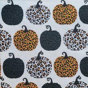 May include: A white background with a repeating pattern of black, orange and white pumpkins with a leopard print design.