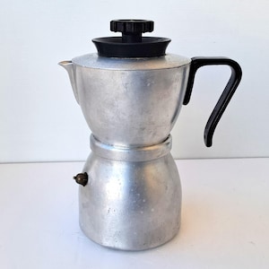 Pode incluir: Uma cafeteira italiana vintage de alumínio com alça e tampa pretas. A cafeteira tem um design clássico, com uma base redonda e um bico para servir. A alça é curvada para facilitar a pega.