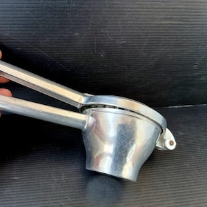 May include: A silver-colored citrus juicer with a hinged design. The juicer has a cup-shaped base and long handles for squeezing. The metal tool is designed for extracting juice from lemons and limes.