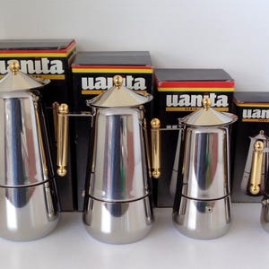 May include: Four stainless steel moka pots of varying sizes, each featuring a polished silver finish, a gold-toned lid knob, and a vertical gold-toned handle. Each coffee maker is positioned in front of its original black box labeled with the brand name Uanita.