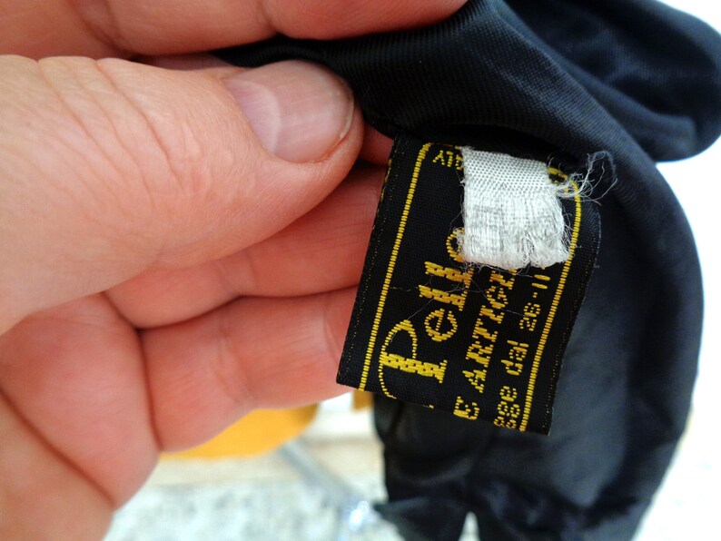 May include: Black leather label with gold stitching and the text "Pelle E. Artigiano" and "asse dal 26-II".