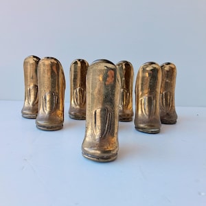 以下が含まれることがあります： 真鍮色のヴィンテージ装飾品8つのコレクション。各オブジェクトは丸みを帯びた上部と前面に垂直の溝があります。オブジェクトは白い表面に配置されています。