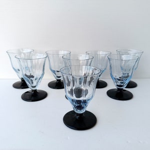May include: Set of eight vintage-style blue-tinted glass goblets with textured sides and black bases. The stemware has a classic design, suitable for serving beverages at a formal dinner or special occasion.