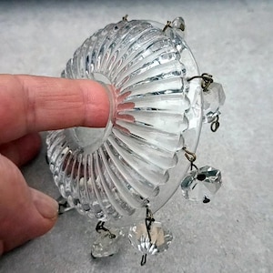 Pode incluir: Peça de lustre de vidro transparente com design canelado e detalhes de cristal pendurados. O vidro tem formato circular com abertura central. Os cristais são facetados e presos com pequenos fios de metal.