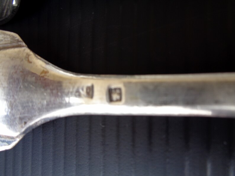 May include: Close-up of the back of a silver spoon with the hallmark "925" stamped on the back.