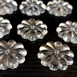Könnte beinhalten: Klare, blütenförmige Verzierungen mit mehreren Blütenblättern sind auf einer dunklen Oberfläche angeordnet. Die transparenten Teile haben ein leicht strukturiertes Aussehen und fangen das Licht ein. Diese dekorativen Elemente könnten für Bastelarbeiten oder zum Verzieren verschiedener Artikel verwendet werden.