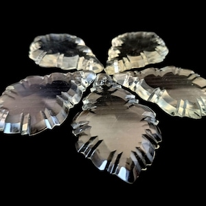 Op de afbeelding: Helder, facetgeslepen kristallen ornamenten in de vorm van bladeren, gerangschikt in een cirkelvormig patroon. Elk ornament heeft een gedetailleerd bladerontwerp met een getextureerde rand. De kristallen zijn transparant.